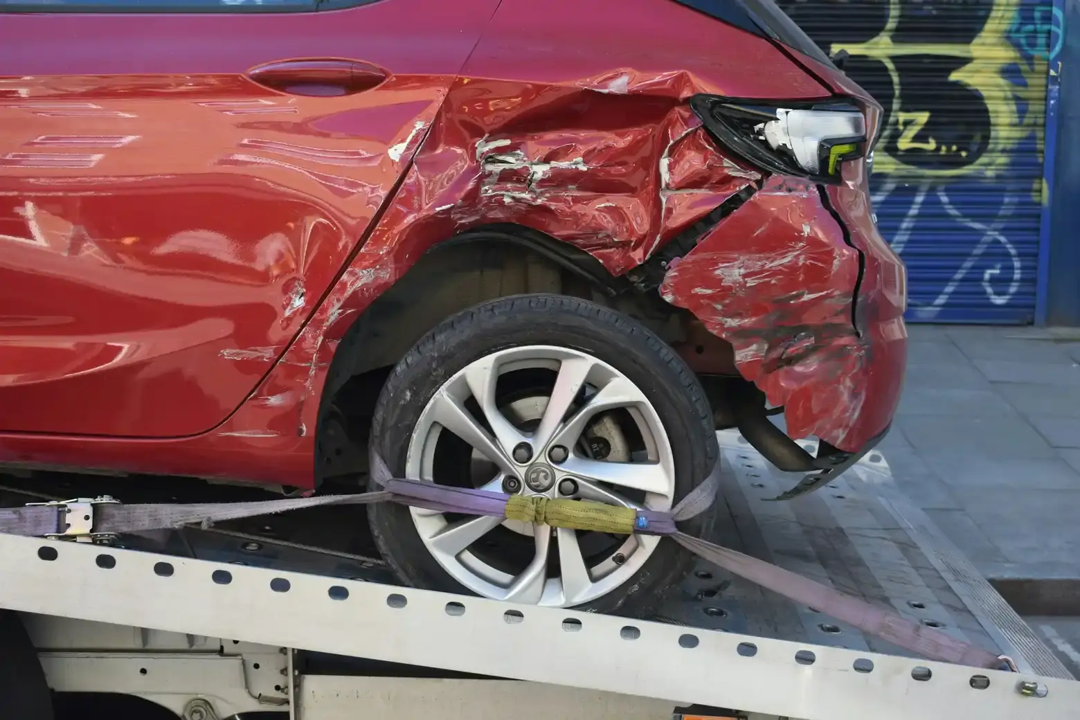 A damaged car strapped down and loaded onto a flatbed tow truck for removal
